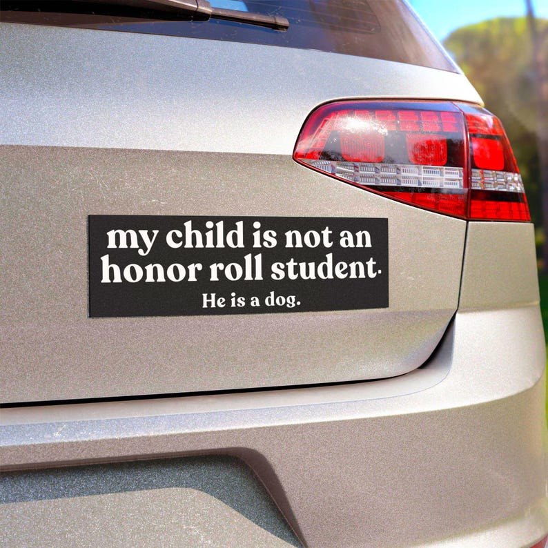 Puede incluir: Una pegatina rectangular negra con texto blanco que dice: "my child is not an honor roll student. He is a dog." La pegatina est&aacute; aplicada en el maletero plateado de un veh&iacute;culo, situada debajo de la ventana trasera y a la izquierda del piloto.