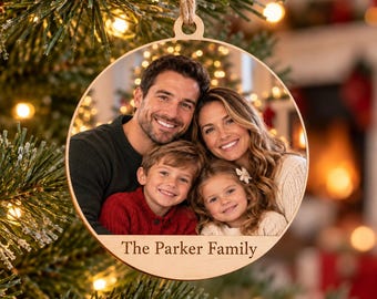 May include: A round wooden Christmas ornament featuring a color photograph of a family of four. The ornament has a light wood border and a jute twine loop for hanging. The text The Parker Family is engraved in a serif font at the bottom.