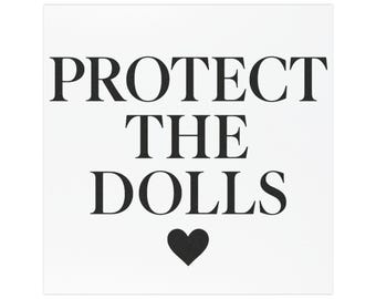 May include: Square white print with the text "PROTECT THE DOLLS" in bold black letters, with a black heart symbol below the text. The design is centered on the print.