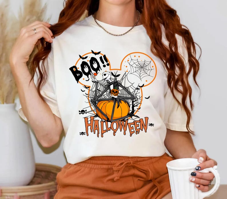 a woman wearing a boo halloween t - shirt holding a cup of coffee