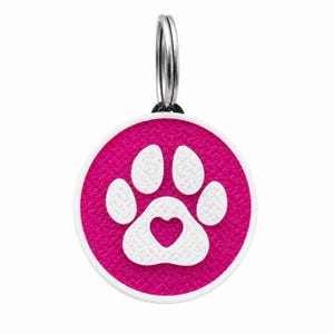 Pode incluir: Uma placa de identificação circular para animais de estimação com um fundo texturizado em rosa vibrante e um design de pata branca. O centro da almofada da pata contém um recorte em forma de coração. A placa tem uma borda branca e um anel.