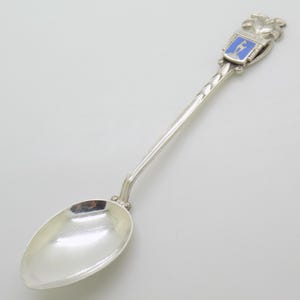 May include: A silver spoon with a detailed handle and a blue and white enamel crest. The spoon has a rounded bowl and a long, slender handle. The crest features a figure and the word "SALZBURG".