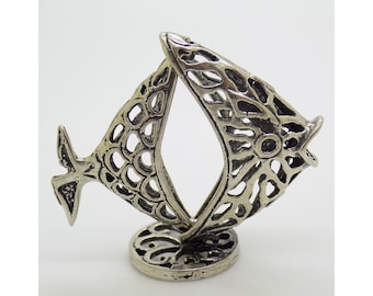 May include: A silver-coloured, openwork fish sculpture. The fish has a detailed, textured design with a circular base. The sculpture is made of metal and has a vintage or antique appearance. The fish is a decorative item.