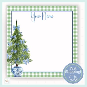 May include: A square notepad with a green and white gingham border and a navy blue inner border. The notepad features a watercolor Christmas tree decorated with blue bows, set in a blue and white vase. The text "Your Name" is written at the top.