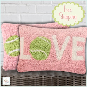 May include: Two pink decorative pillows with a tennis ball design and the word "LOVE" in white. The tennis balls are green and white. The pillows are made of a textured material.