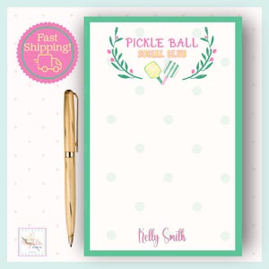 Op de afbeelding: Een gouden pen ligt naast een notitieblok met een turquoise rand. Het notitieblok toont de tekst "Pickle Ball Social Club" met een bloemmotief en de naam "Kelly Smith". De achtergrond is wit met turquoise stippen.