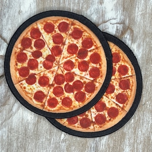 May include: Two round black and white coasters with a pepperoni pizza design. The coasters are made of fabric and have a black border.