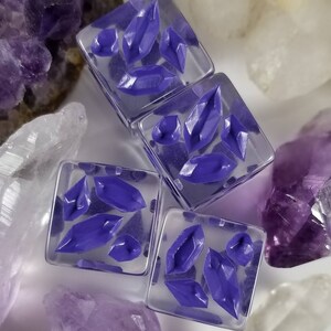 May include: Four square, clear resin beads with embedded purple crystal shapes. The beads are surrounded by amethyst and quartz crystals. The crystals within the beads have a faceted design, creating a sparkling effect.