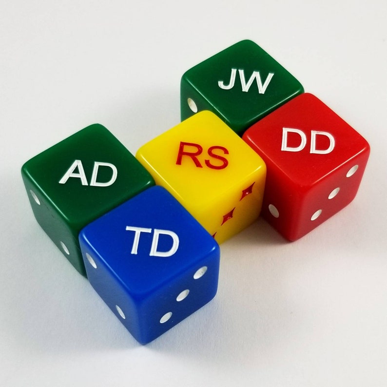 May include: Four colorful dice with white letters on each side. The dice are green, yellow, red, and blue. The letters on the dice spell out "AD", "RS", "DD", and "TD".