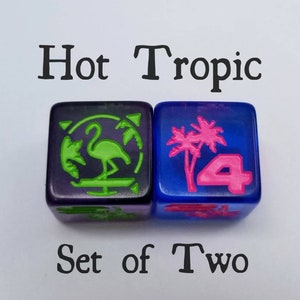May include: Set of two dice with a tropical theme. One die is purple with a green flamingo and palm tree, the other is blue with a pink palm tree and the number 4.