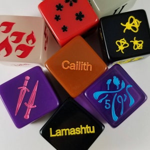 May include: A set of ten-sided dice with various colors and designs. The dice feature different symbols and text, including "Caillith" and "Lamashu".