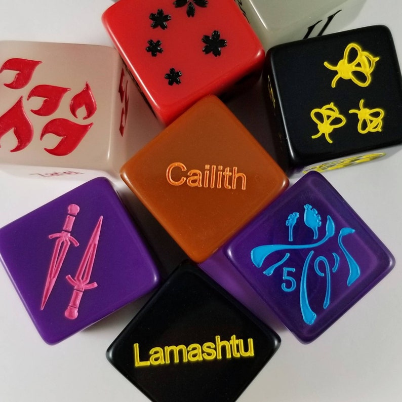 May include: A set of ten-sided dice with various colors and designs. The dice feature different symbols and text, including "Caillith" and "Lamashu".