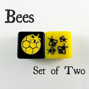 May include: Set of two black and yellow dice with bee designs. One die has a honeycomb with a bee on top. The other die has five bees.