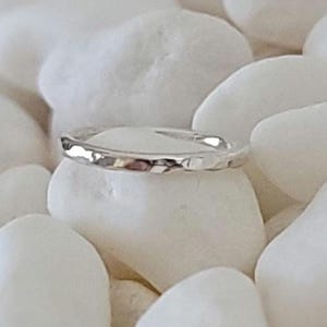 May include: A silver ring with a textured, hammered design. The ring is set against a backdrop of smooth, white stones. The ring's surface reflects light, highlighting its unique texture. Jewellery.