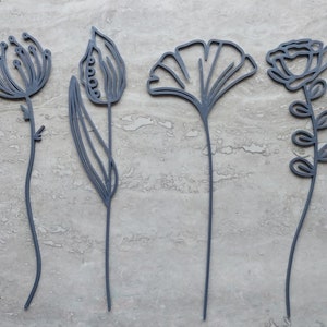 Op de afbeelding: Vier metalen bloemen uitsnijdingen in zwart, waaronder een tulp, een ginkgo blad, een roos en een wilde bloem.