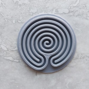 May include: A gray plastic circular labyrinth with a spiral design.