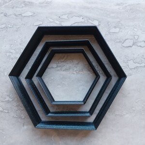 May include: Three black hexagonal cookie cutters of different sizes, nested inside each other.