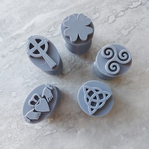 Puede incluir: Cinco sellos de goma grises con diferentes símbolos irlandeses. Los símbolos incluyen un trébol, un nudo celta, un nudo de la trinidad, un anillo Claddagh y una cruz celta.