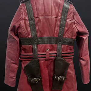 May include: A burgundy leather jacket with black accents, featuring a high collar, shoulder epaulets, and a belted waist. The jacket has two attached holster-like pockets with buckle closures, and padded shoulder details.