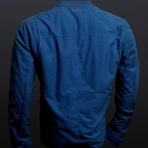 May include: A blue jacket with long sleeves and a mandarin collar. The back of the jacket is visible, showcasing the tailored seams and a subtle pocket detail. The jacket is made of a textured fabric.
