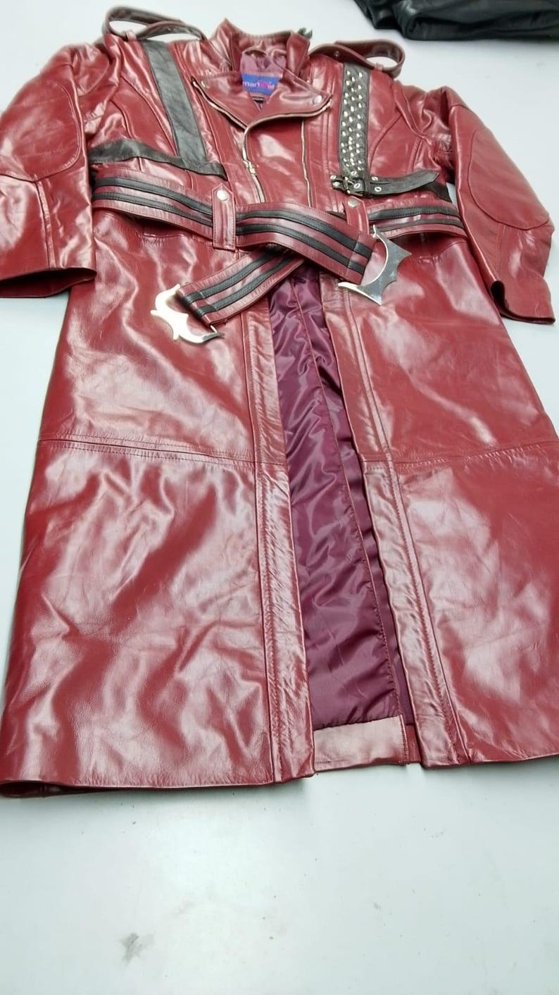 May include: A burgundy leather coat with a belted waist and black accents. The coat features a zipper closure, studded details, and a burgundy lining. The coat is a long length and has a classic, edgy style.