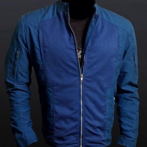 May include: A blue jacket with a full-length zipper and a stand-up collar. The jacket has a textured, ribbed design on the front and smooth panels on the shoulders and sleeves. It features two zippered pockets on the sleeves.