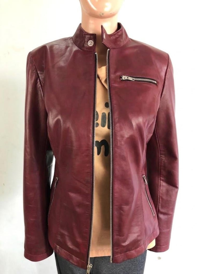 May include: A burgundy leather jacket with a stand-up collar and a silver zipper closure. The jacket has two zippered pockets and a tailored fit. The jacket is shown on a mannequin.