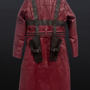 May include: A burgundy leather coat with black accents. The coat features a long design with a belted waist, shoulder straps, and two small pockets with buckles. The back of the coat is visible, showcasing the detailed stitching and design.