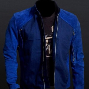 May include: A blue suede leather jacket with a zip-up front and a stand-up collar. The jacket has a two-tone design, with a darker blue on the body and a lighter blue on the shoulders and sleeves. The text "Suede Leather" is at the top.