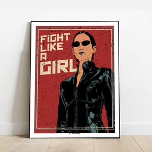 Peut inclure: Une affiche rouge et blanche avec une femme portant une veste en cuir noire et des lunettes de soleil. L'affiche dit "Fight Like A Girl".