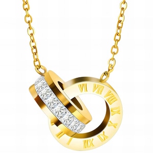 Könnte beinhalten: Eine goldfarbene Halskette mit zwei ineinandergreifenden Ringen. Ein Ring ist mit einer Reihe klarer, funkelnder Kristalle besetzt. Der andere Ring hat römische Ziffern um seinen Umfang graviert. Die Halskette hängt an einer zarten Kette.