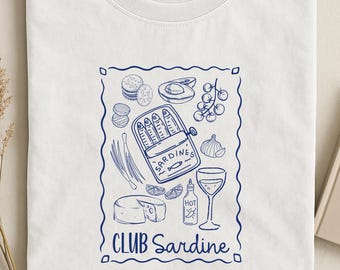 May include: A white t-shirt featuring a blue line-art graphic of a sardine tin, crackers, avocado, cherry tomatoes, garlic, cheese, hot sauce, and a wine glass. The text reads "SARDINES" on the tin and "CLUB Sardine" at the bottom of the frame.