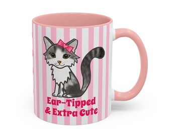 May include: A ceramic mug with a pink handle and interior, featuring a white and pink vertical striped pattern. The front displays a gray and white cat illustration with a pink bow and the text Ear-Tipped & Extra Cute in pink lettering.