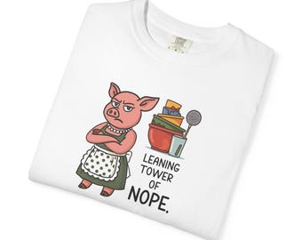 May include: A white t-shirt featuring a graphic of a pink pig wearing a green apron and a pearl necklace, standing with arms crossed next to a stack of colorful kitchen bowls and utensils, with the text LEANING TOWER OF NOPE. printed below.