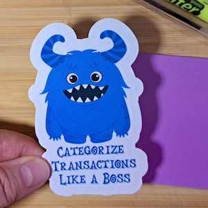 May include: A blue monster sticker with the text "CATEGORIZE TRANSACTIONS LIKE A BOSS." The sticker features a cartoon monster with large eyes, a wide grin, and curly horns. The sticker is on a white background.