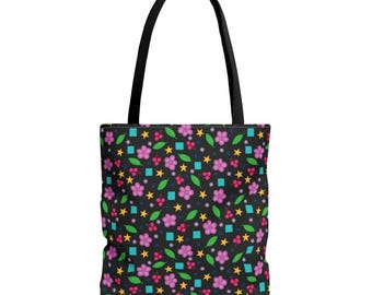 May include: A black tote bag featuring a repeating pattern of pink five-petaled flowers, yellow four-pointed stars, green leaves, small red berry clusters, and light blue squares. The bag has two black fabric shoulder straps attached at the top.