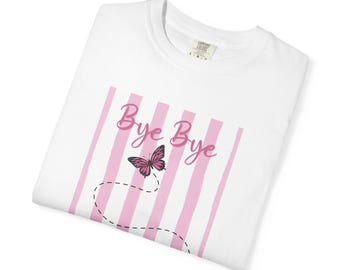 May include: A white t-shirt featuring a graphic of vertical light pink stripes. The design includes the text "Bye Bye" in a pink script font, accompanied by a pink and black butterfly illustration with a dashed black line trailing behind it.