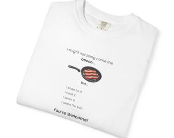 May include: A white t-shirt featuring a graphic of a black frying pan with bacon strips inside. The text reads: I might not bring home the bacon.... But... I shop for it, I cook it, I serve it, I clean the pan, You're Welcome!