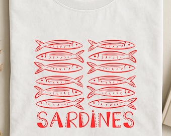 May include: A white t-shirt featuring a graphic print of twelve red sardines arranged in two columns of six. Below the fish, the word SARDINES is printed in a bold, red, decorative font. The shirt has a crew neckline and a Comfort Colors brand label.