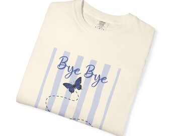 May include: A cream-colored t-shirt featuring a graphic of vertical light blue stripes, a blue butterfly, and the text "Bye Bye" in blue script. A dashed black line traces a path behind the butterfly on the front of the garment.