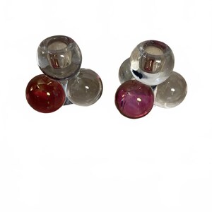 May include: Two glass candle holders, each composed of three clear spheres and one colored sphere. One holder has a red sphere, the other a purple sphere. The candle holders have a modern, minimalist design.