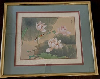 May include: Framed artwork featuring a hummingbird hovering near pink lotus flowers and green lily pads. The artwork has a gold frame with a green and brown matting, creating a serene and natural scene.