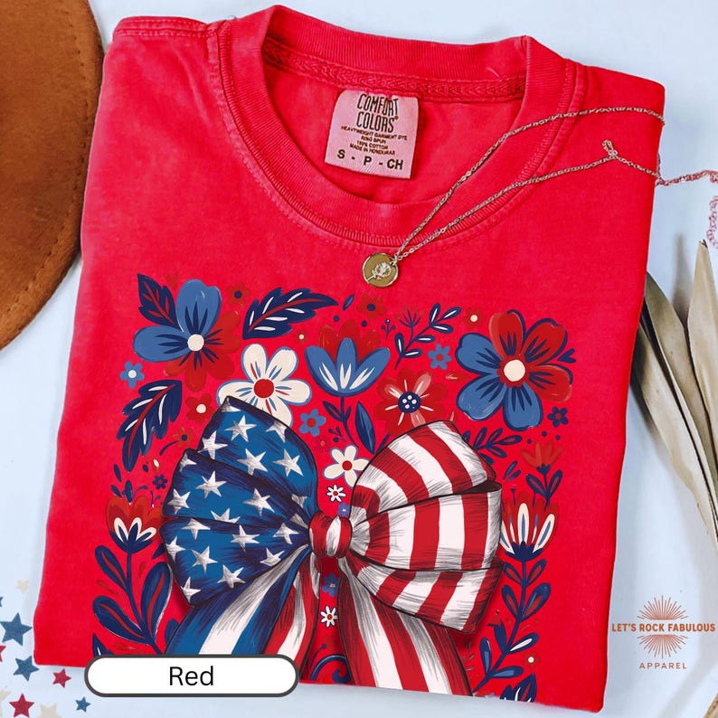 Boho floral American flag bow t-shirt on Comfort Colors 1717 unisex tee. Patriotic 4th of July shirt for women featuring red white and blue bow with floral design. Available in sizes S, M, L, XL, 2XL, 3XL, 4XL and multiple color options including ivory, white, navy, pepper, blossom, and chambray. Perfect America 250th Anniversary tee, Independence Day outfit, summer BBQ, and casual Americana style.