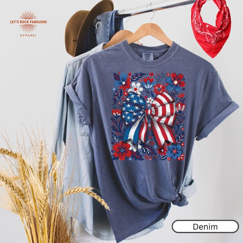 Boho floral American flag bow t-shirt on Comfort Colors 1717 unisex tee. Patriotic 4th of July shirt for women featuring red white and blue bow with floral design. Available in sizes S, M, L, XL, 2XL, 3XL, 4XL and multiple color options including blue, ivory, white, navy, pepper, blossom, and chambray. Perfect 250th Anniversary tee, Independence Day outfit, summer BBQ, and casual Americana style.