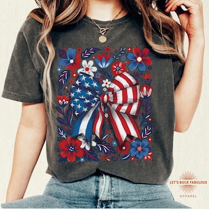 Boho floral American flag bow t-shirt on Comfort Colors 1717 unisex tee. Patriotic 4th of July shirt for women featuring red white and blue bow with floral design. Available in sizes S, M, L, XL, 2XL, 3XL, 4XL and multiple color options including ivory, white, navy, pepper, blossom, and chambray. Perfect America 250th Anniversary tee, Independence Day outfit, summer BBQ, and casual Americana style.