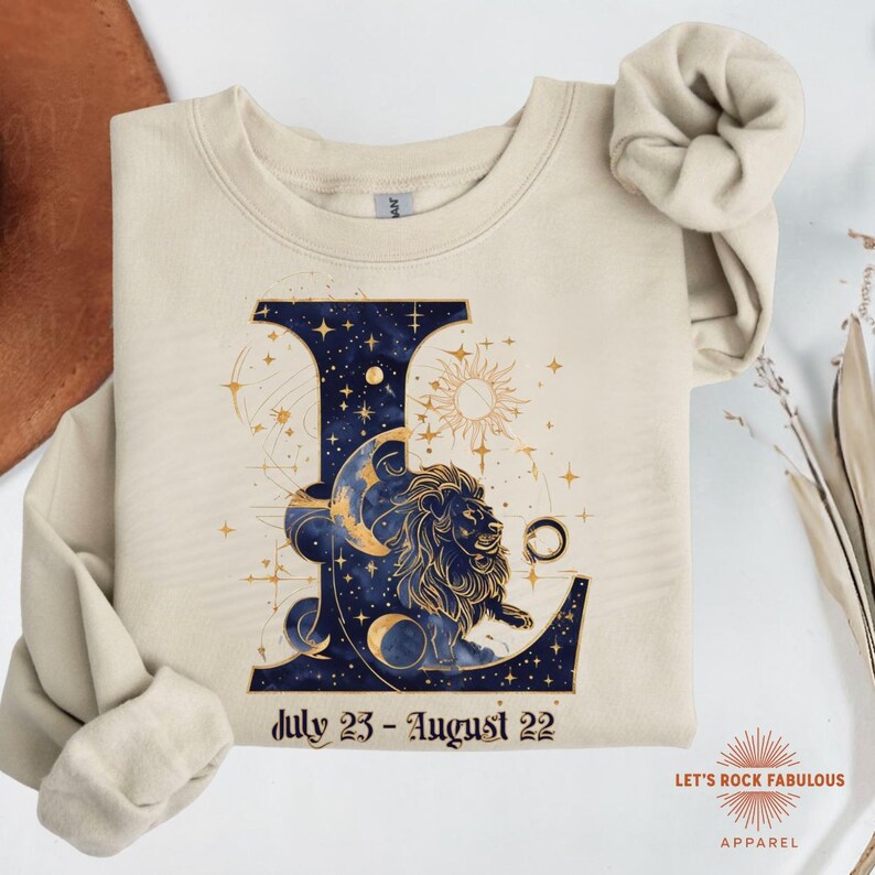 Leo Zodiac Sign celestial lion graphic on a Gildan sweatshirt featuring gold moon phases, stars, and cosmic artwork with July 23–August 22 text. Astrology-inspired graphic crewneck available in multiple colors and sizes S to 4XL. Perfect gift for Leo birthdays, horoscope lovers, and boho celestial fashion.