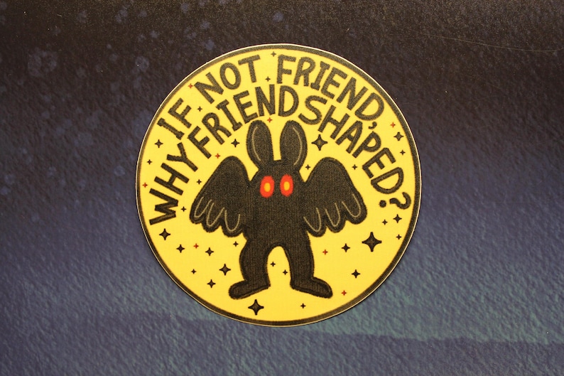 K&ouml;nnte beinhalten: Ein gelber runder Aufkleber mit einer schwarzen Fledermaus-&auml;hnlichen Kreatur mit roten Augen und dem Text "WHY IF NOT FRIEND SHAPED?" in Schwarz.
