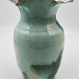 Peut inclure: Un vase en céramique fait à la main avec un bord unique et froncé. Le vase présente un glaçage vert-bleu clair avec des accents vert foncé et marron. Ce vase décoratif est idéal pour exposer des fleurs ou comme objet d'art.