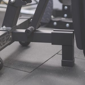 Puede incluir: Banco de pesas negro con asiento y respaldo acolchados, con el logotipo de REP en el marco. El banco tiene cuatro ruedas para facilitar la movilidad y patas ajustables.