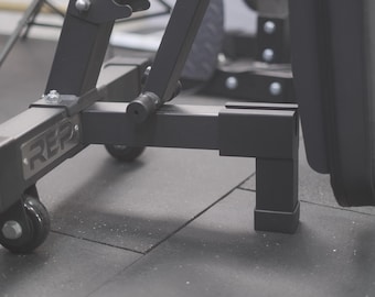 May include: Black weight bench with a padded seat and back, featuring a REP logo on the frame. The bench has four wheels for easy mobility and adjustable legs.